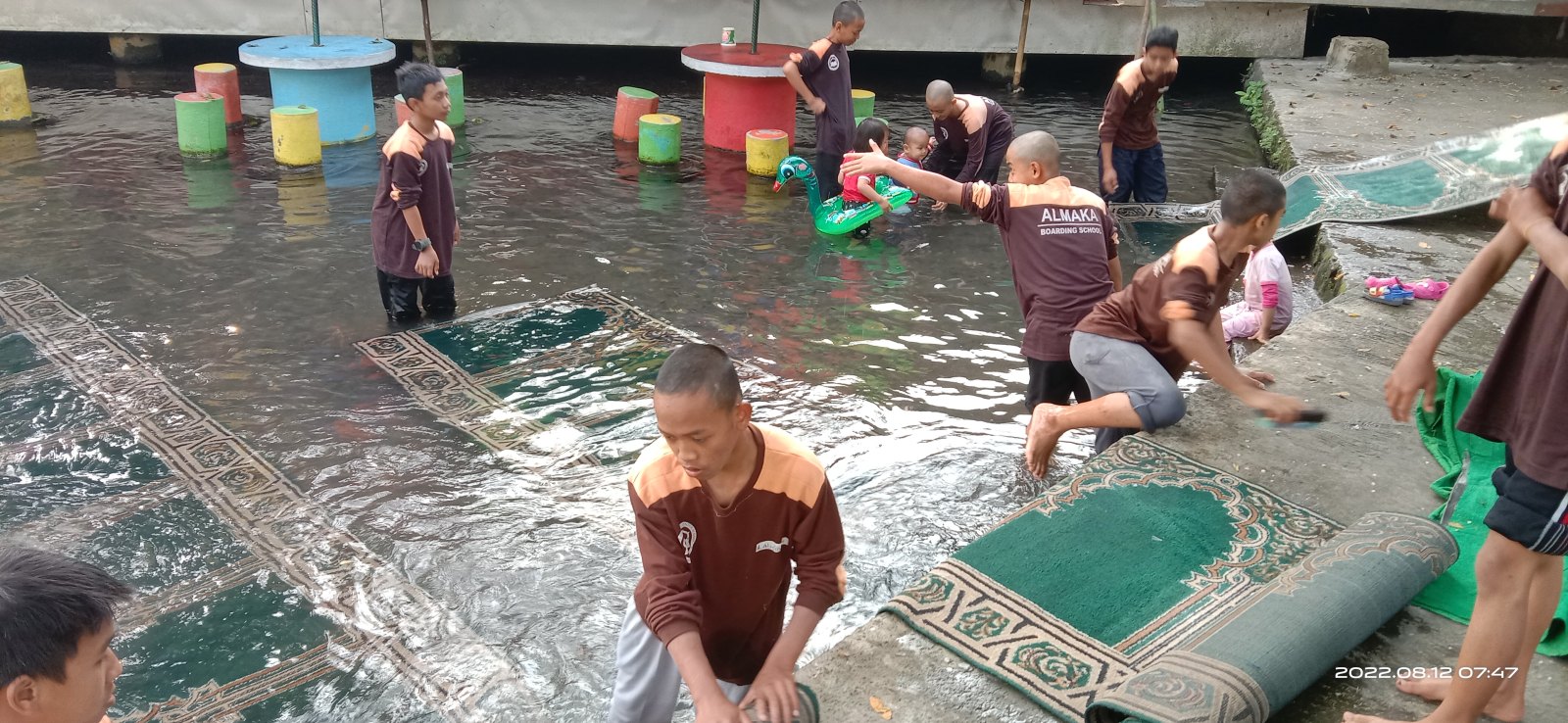 Santri dan ustadz bersama-sama mencuci karpet masjid di kolam