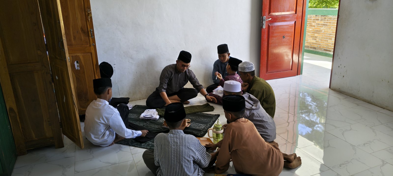Ustadz Salman duduk bersama santri mengajari cara melipat dan menata lemari