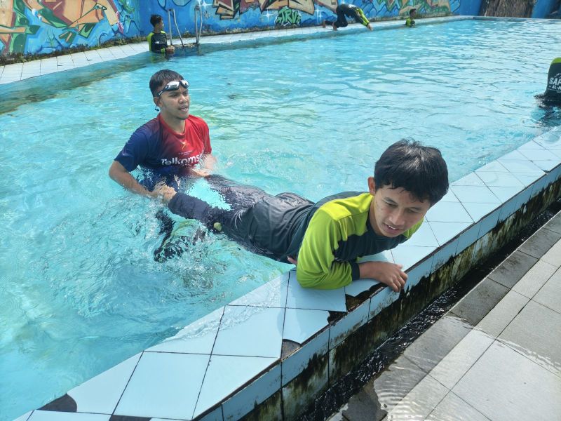 Ustadz Salman memegangi kaki santri yang berlatih renang di tepi kolam