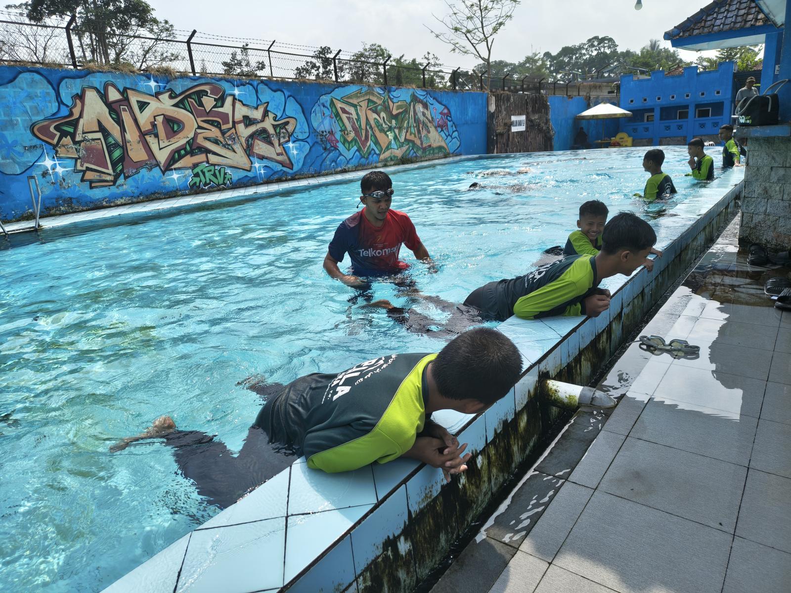 Santri berpegangan di tepi kolam sambil melatih gerakan kaki, diawasi Ustadz Salman